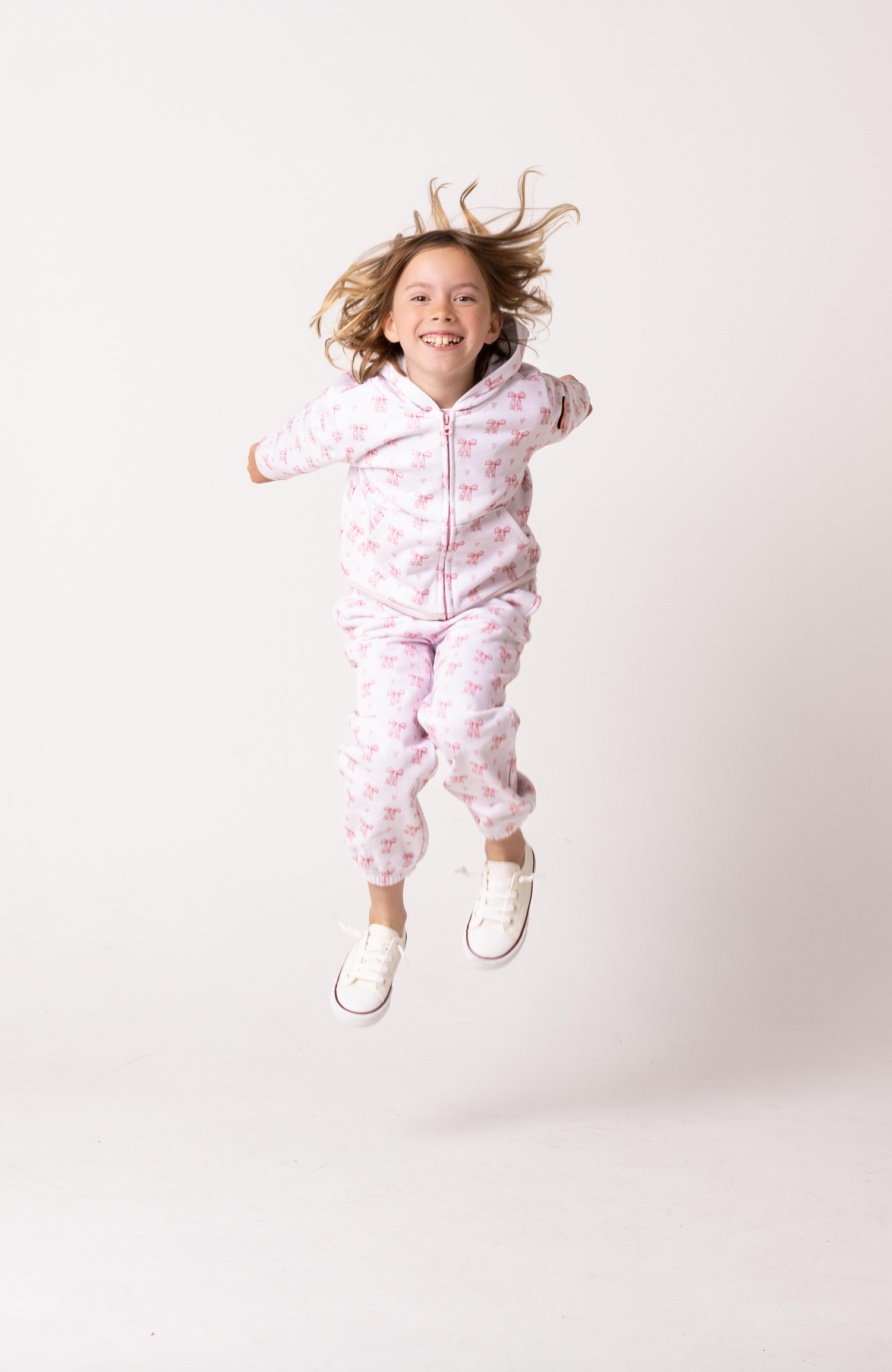 Child in a pink sweatsuit jumping against a white background